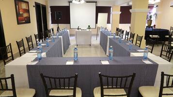 Un salón de conferencias con una larga mesa, sillas y una pantalla de proyector.