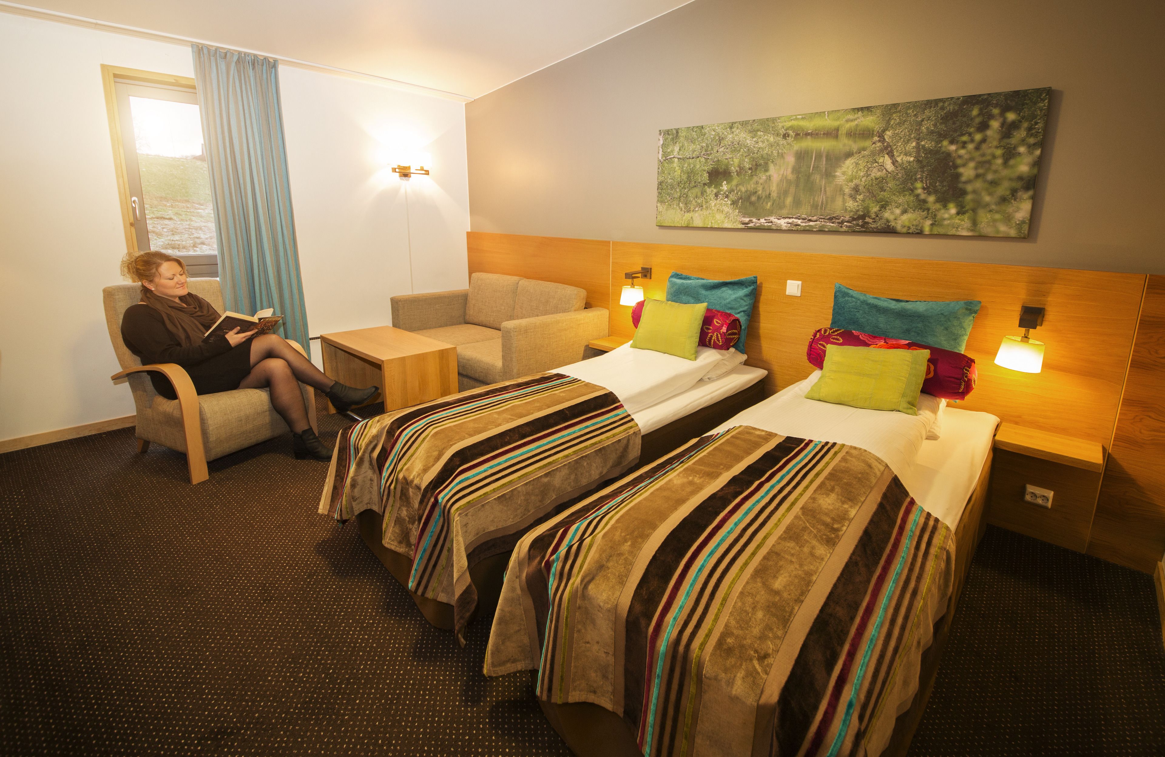 A hotel room with two single beds, a sofa, a small table, and a window with curtains.