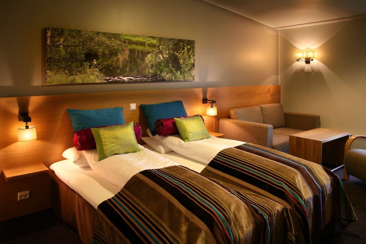 A hotel room with two beds, a sofa, a small table, and a wall-mounted painting.