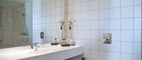 Un baño moderno con un espejo grande, dos lavamanos, ducha y váter.