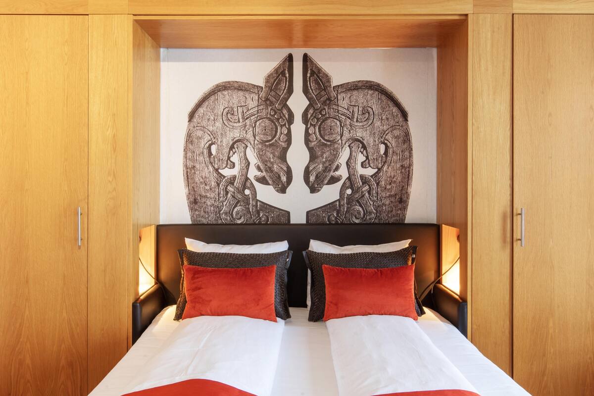 A bed with a white and red bedspread, two red pillows, and a headboard with a symmetrical design.
