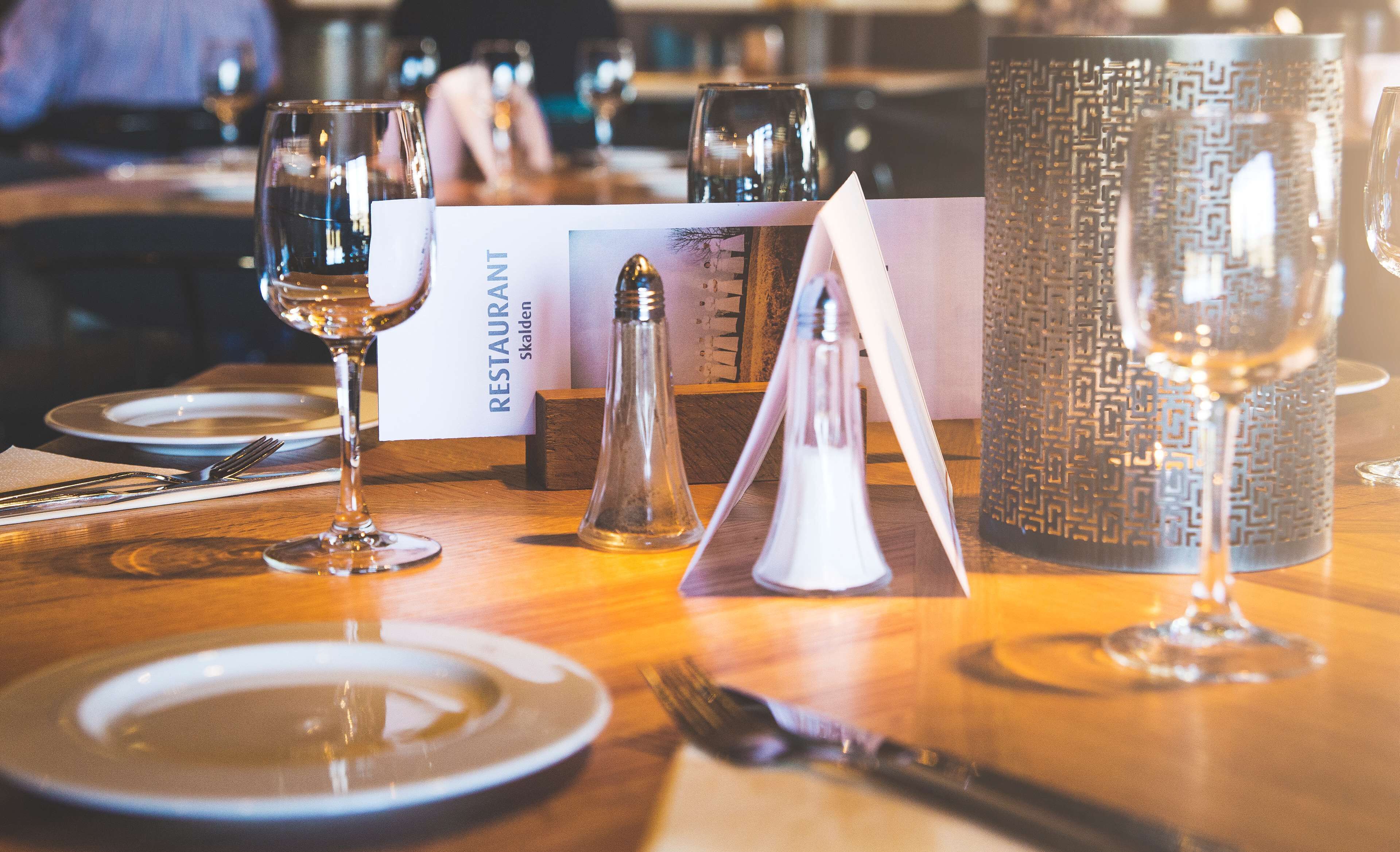 Una mesa de restaurante dispuesta con platos, cubiertos, vasos y una carta.