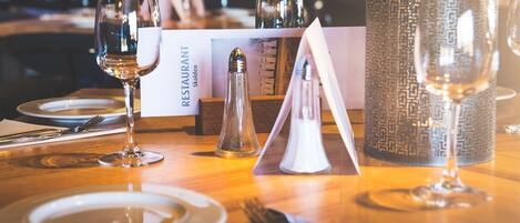 Una mesa de restaurante dispuesta con platos, cubiertos, vasos y una carta.