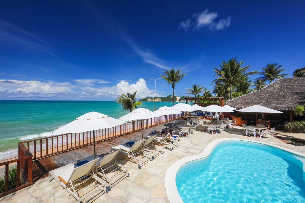 A poolside area with lounge chairs and umbrellas, overlooking a beach and ocean.
