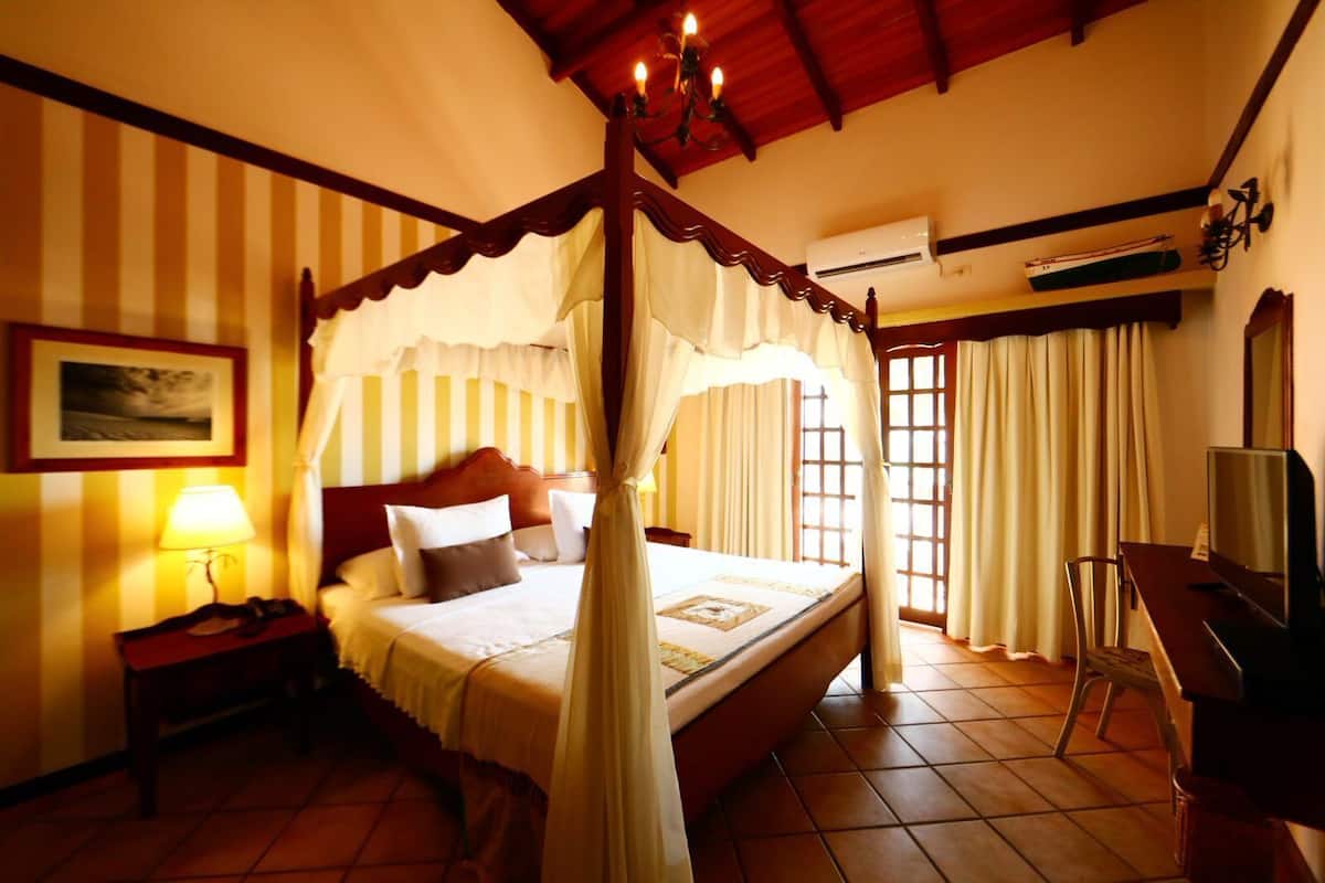 A four-poster bed with a canopy, a bedside table with a lamp, a television, and a chair.