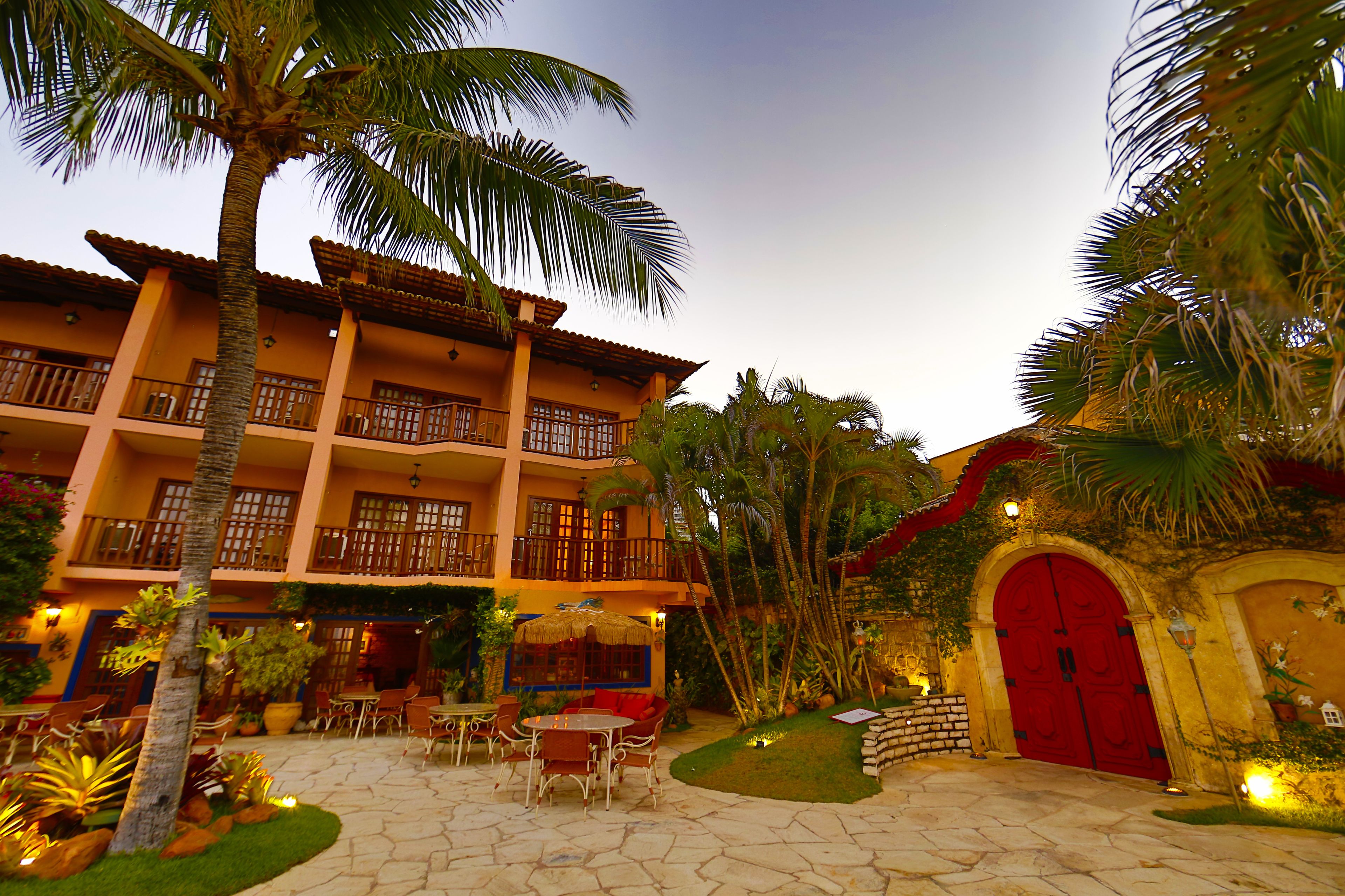 A hotel courtyard with outdoor seating, palm trees, and a red door.