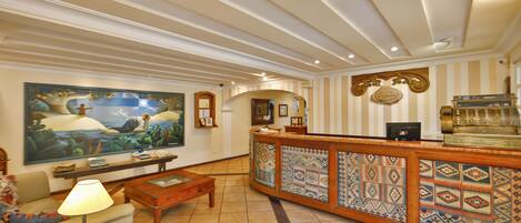 A lobby with a reception desk, a painting, a sofa, a lamp, and a coffee table.