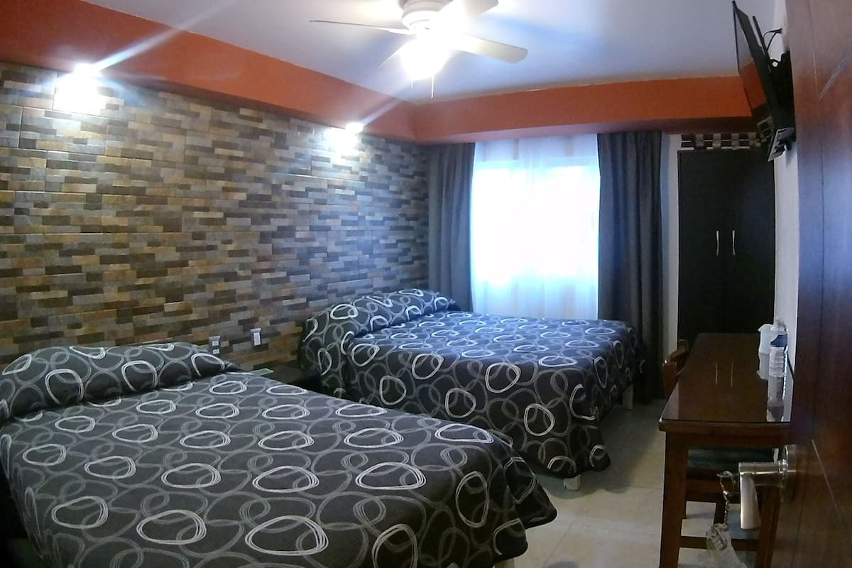 Ein Hotelzimmer mit zwei Betten, einem Holztisch, einem Deckenventilator und einer Wand mit Ziegeloptik.