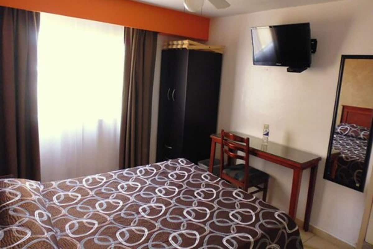 Ein Hotelzimmer mit zwei Betten, einem Schreibtisch, einem Sessel, einem Fernseher und einem Kleiderschrank.