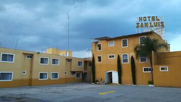 A yellow building with a sign reading "HOTEL SAN LUIS" and a parking lot in front.