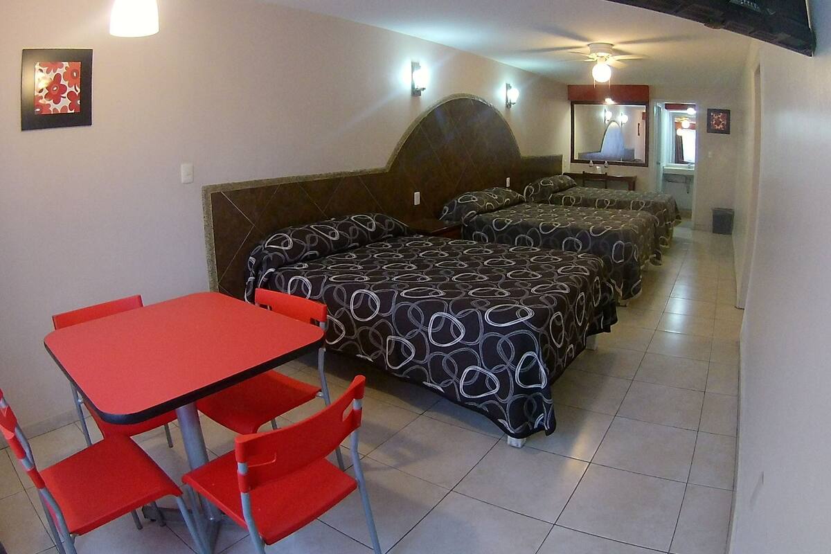 Ein Hotelzimmer mit einem Einzelbett, einem kleinen Tisch mit zwei Stühlen und einem großen Bett mit einem gemusterten Überwurf.