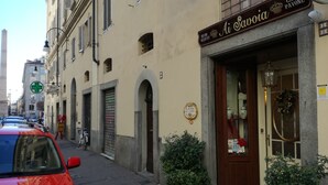 A street view with a building labeled "Ai Savoiia" indicating a bed and breakfast. There are parked cars, a bicycle, and a green cross sign on the left. - Ai Savoia B&B - Guest House  (Turin)