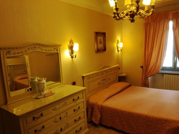 A bedroom with a bed, dresser, mirror, wall sconces, and a window with curtains. - Ai Savoia B&B - Guest House (Turin)