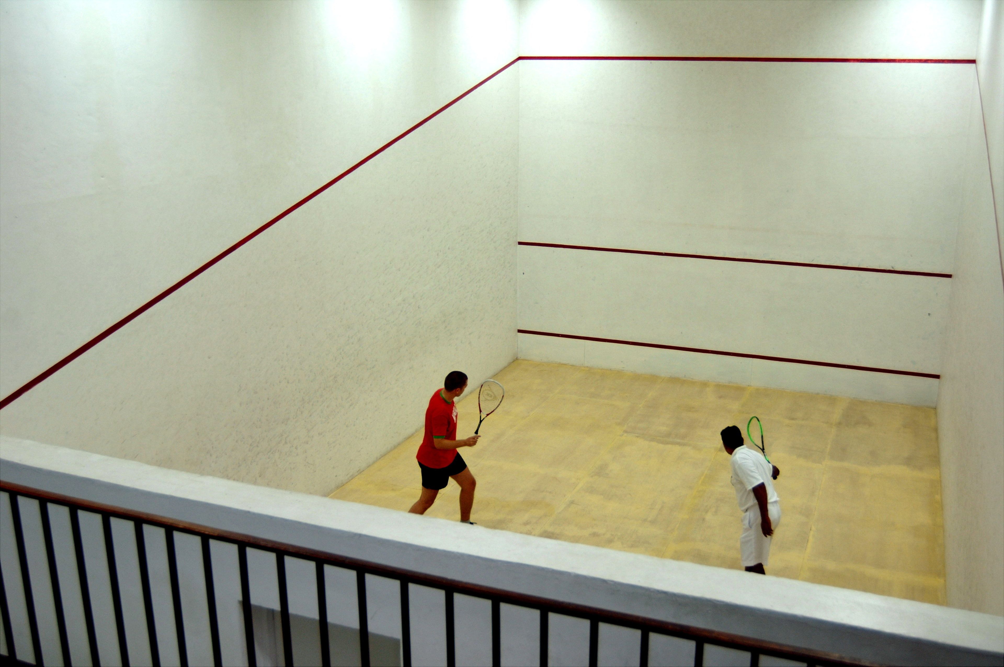 A squash court with a white wall and a wooden floor.