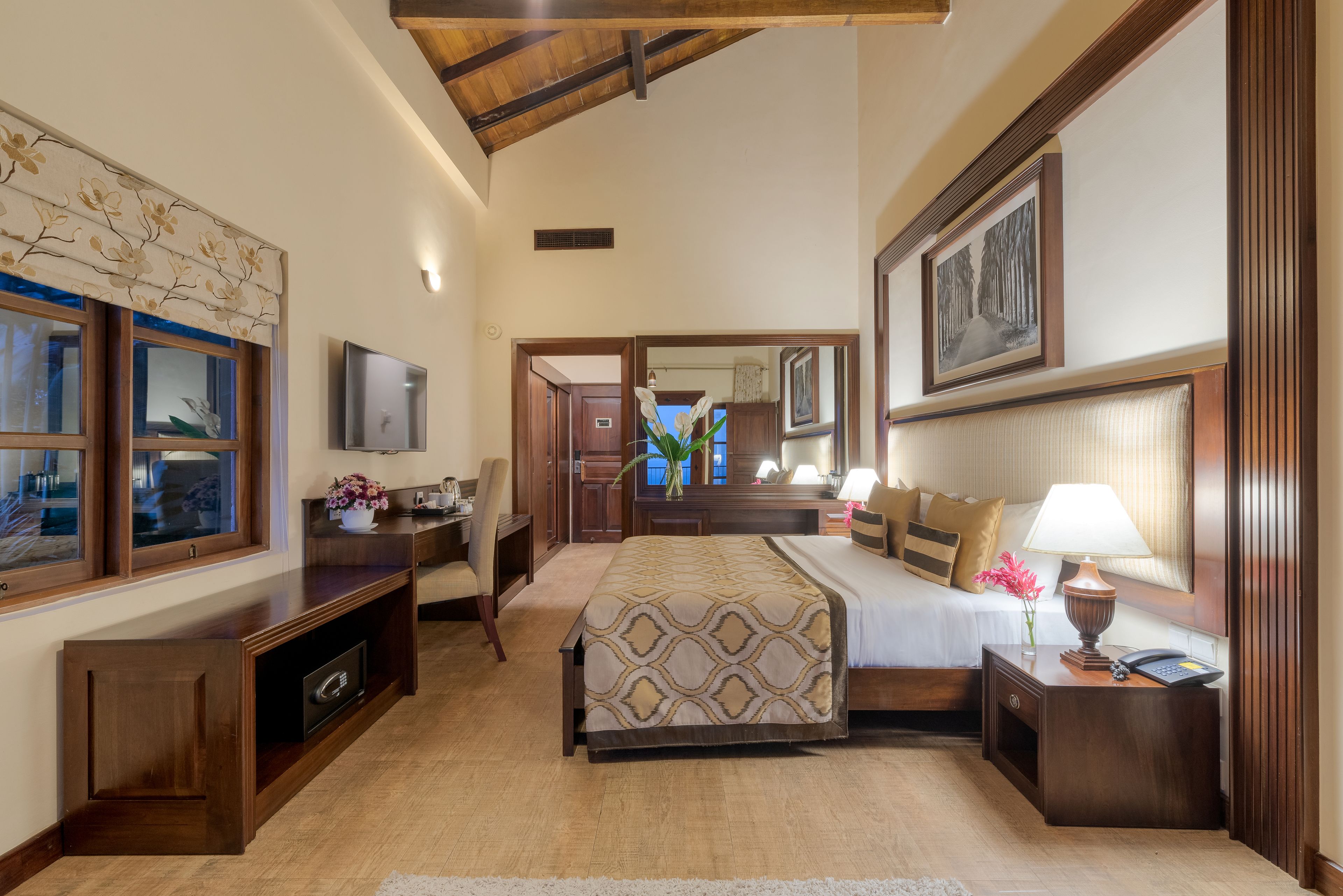 A spacious bedroom with a large bed, a desk, a chair, a TV, and a mirror.