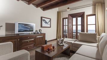 Una sala de estar moderna con techo de madera, televisor de pantalla plana, una mesa de centro de madera con frutas y un sofá color beige.