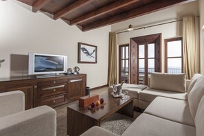 A modern living room with a wooden ceiling, a flat-screen TV, a wooden coffee table with fruits, and a beige sofa.