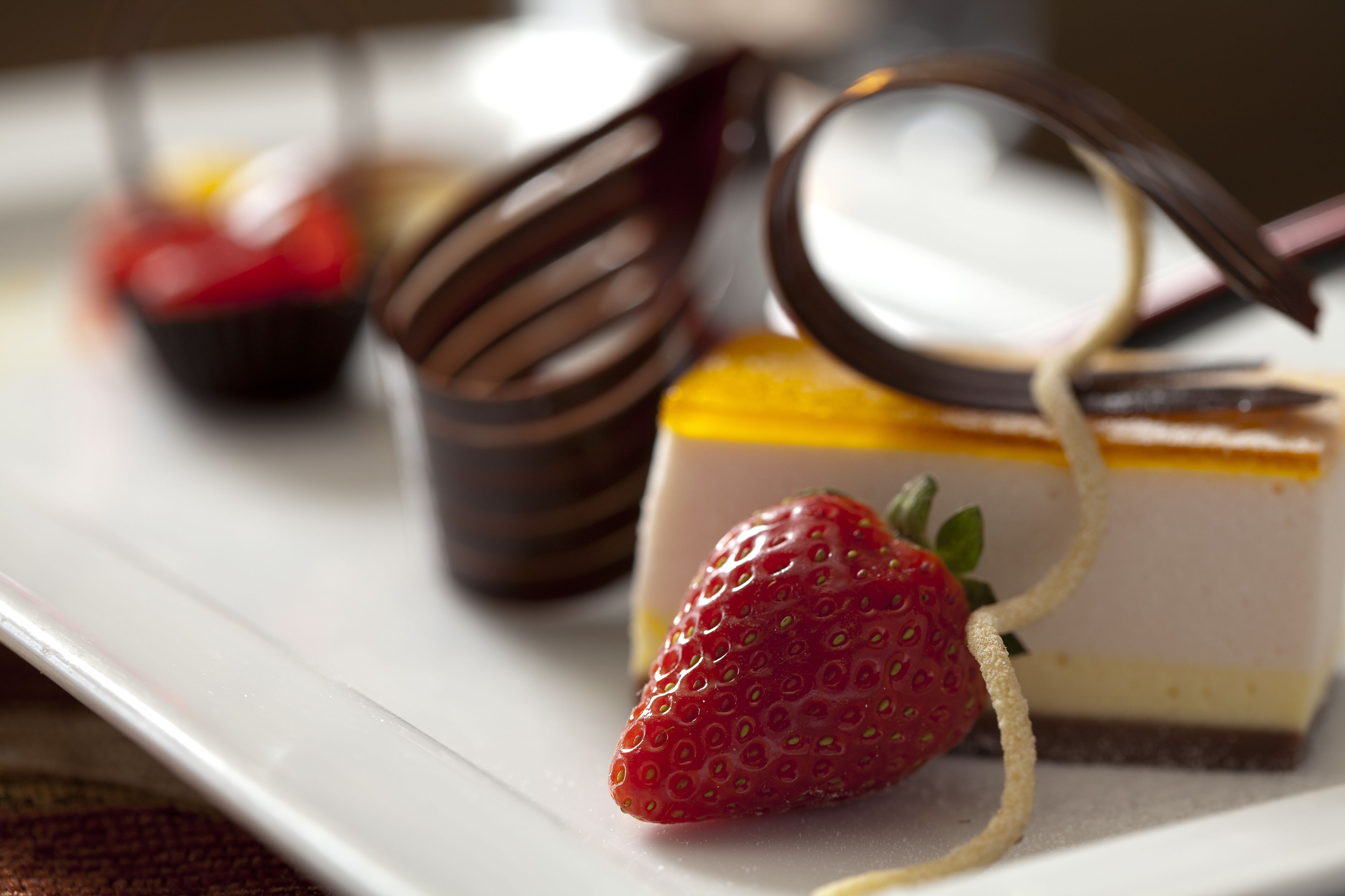 A dessert plate with a layered cake, a chocolate-covered fork, and a strawberry.