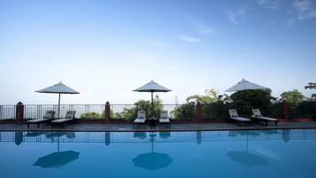 A swimming pool with lounge chairs and umbrellas, surrounded by a fence and trees.