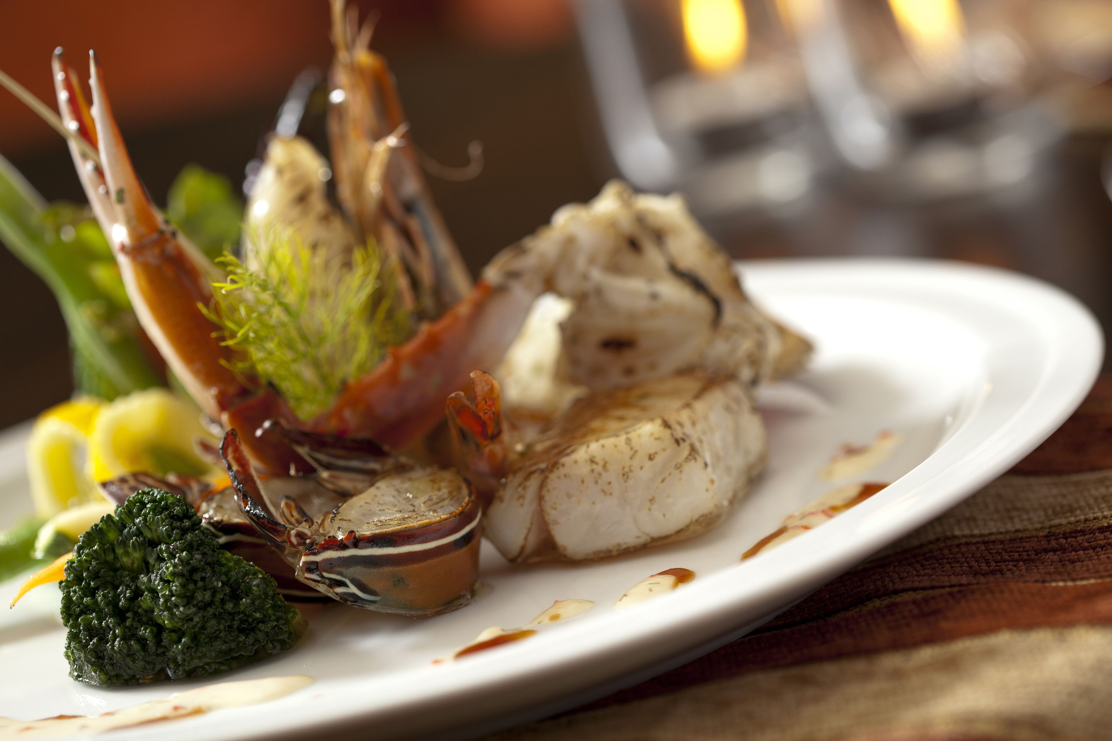 A plate of seafood including a lobster, fish, and broccoli.
