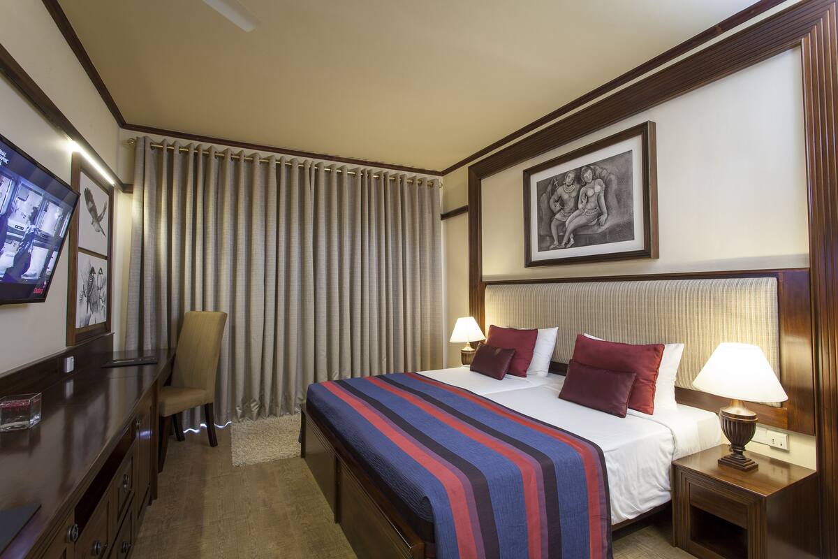 A hotel room with a large bed, a desk with a chair, a television, and a framed picture on the wall.
