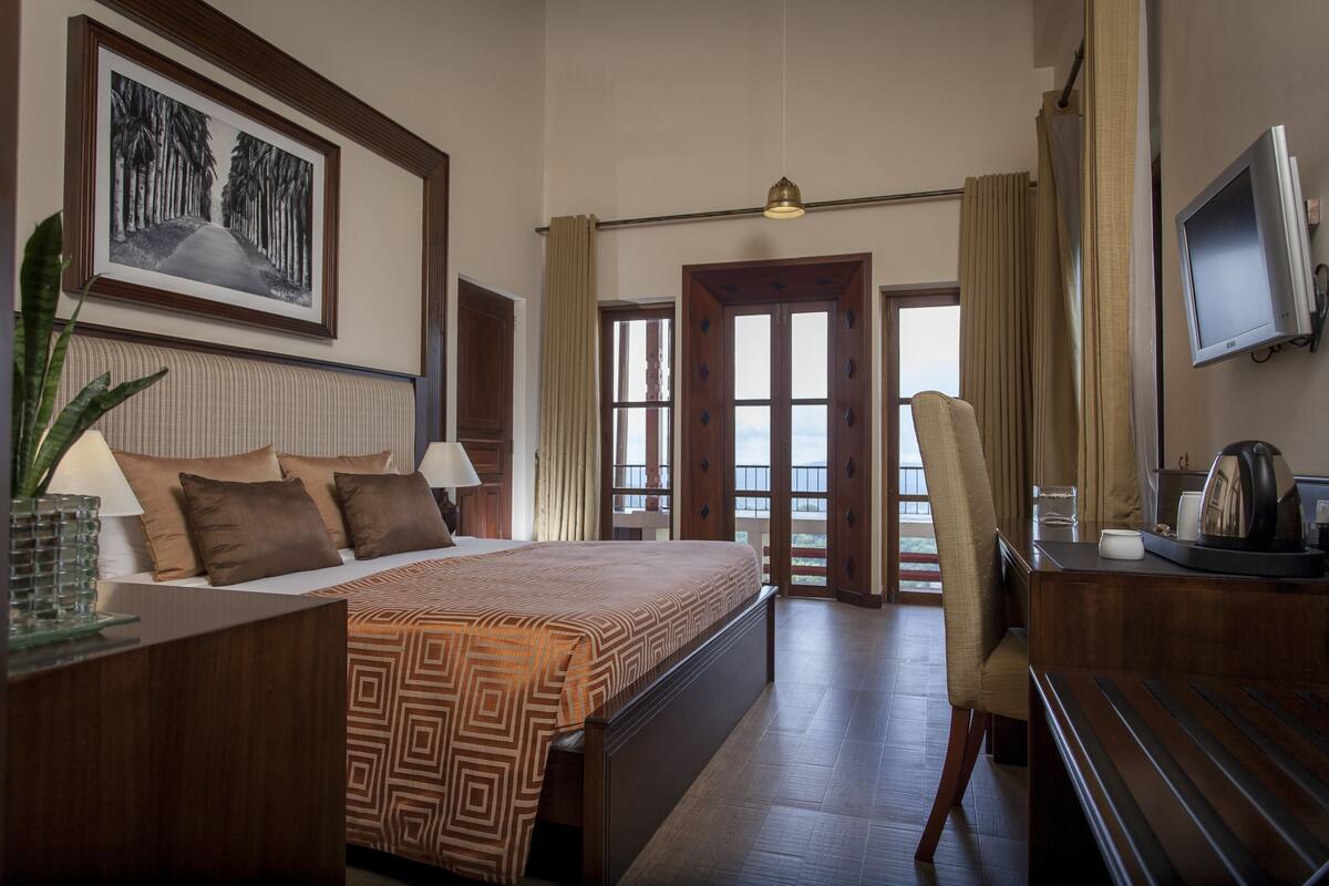 A hotel room with a large bed, a desk with a chair, a television, and a large window with curtains.