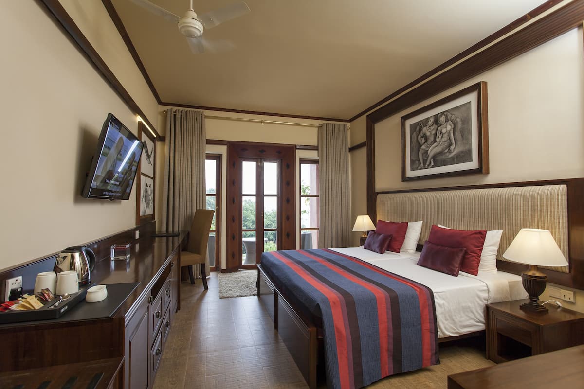 A hotel room with a large bed, bedside tables, a TV, and a view of the outdoors through the door.