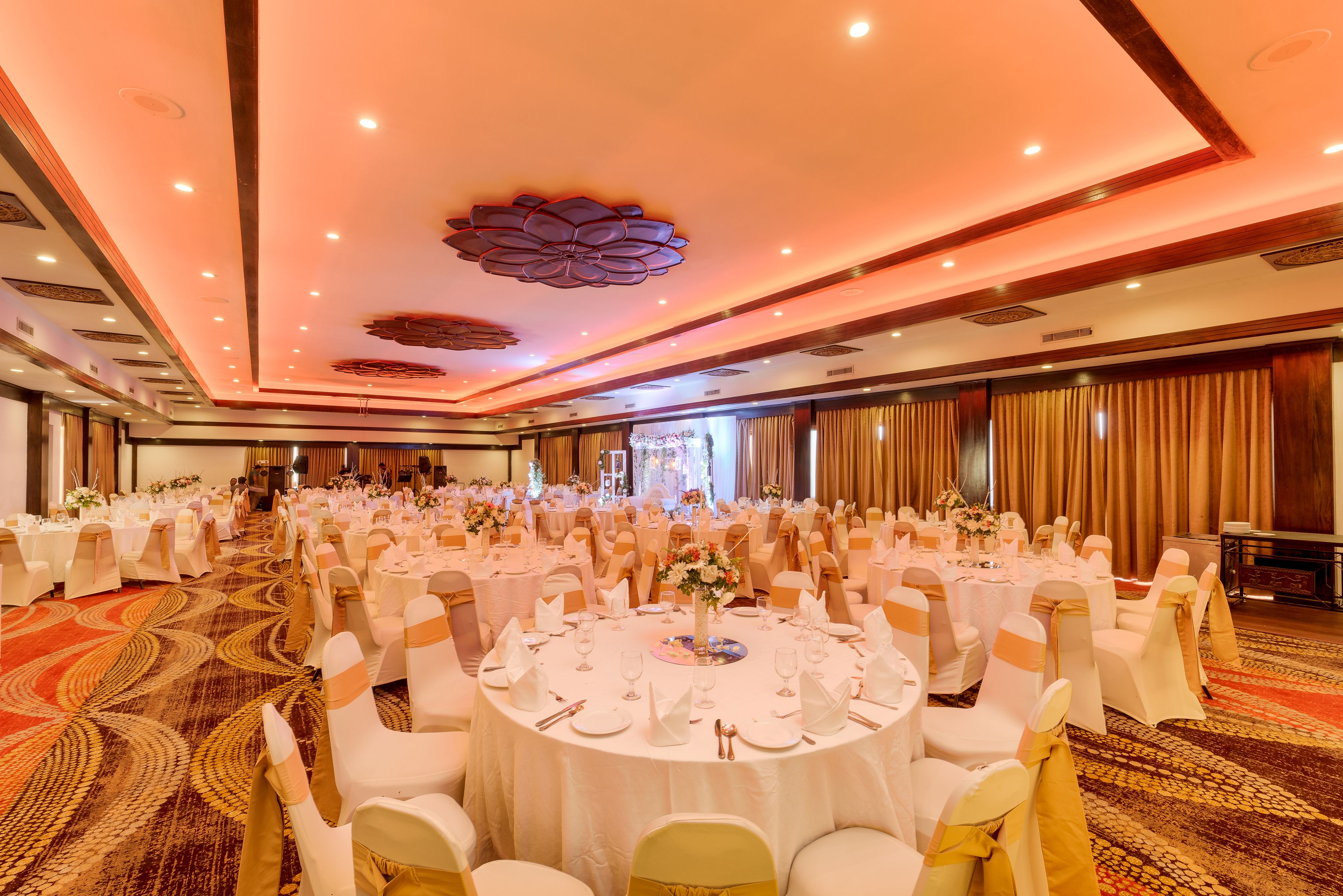A banquet hall with round tables set for a formal event, featuring a carpeted floor and a decorative ceiling.