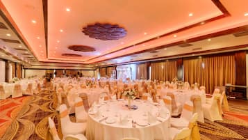 A banquet hall with round tables set for a formal event, featuring a carpeted floor and a decorative ceiling.