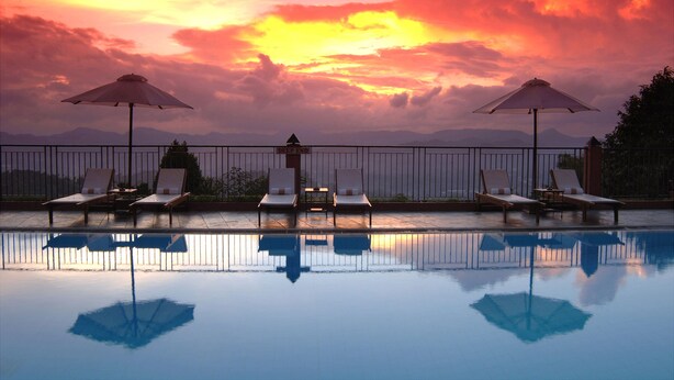 A poolside area with lounge chairs and umbrellas, reflecting the sunset sky. - Amaya Hills Kandy (Kandy)
