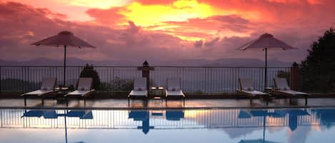 Una piscina al aire libre, sombrillas, sillones reclinables de piscina