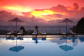 A poolside area with lounge chairs and umbrellas, reflecting the sunset sky. - Amaya Hills Kandy (Kandy)