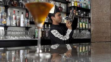 A bar with a bartender preparing a drink, shelves stocked with various bottles, and a glass of cocktail in the foreground.