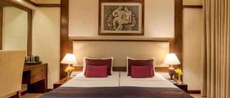 A hotel room with a large bed, two bedside tables with lamps, a desk, and a framed artwork on the wall.