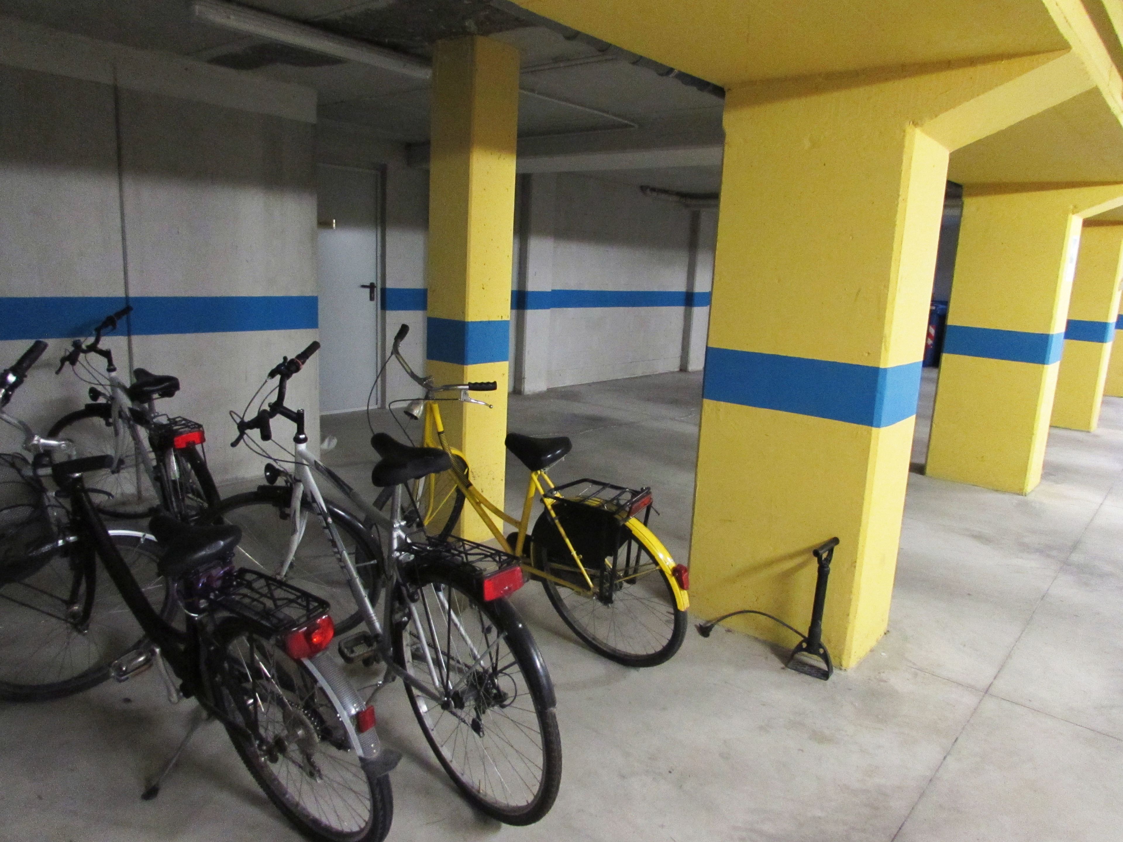 A parking garage with yellow pillars and blue stripes, containing several bicycles parked against the walls.