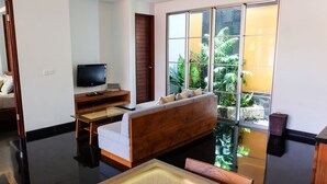 A modern hotel room with a bed, a TV, a desk, a sofa, and a large window with a view of greenery. - Sun Island Boutique Villas & Spa Seminyak (Seminyak)