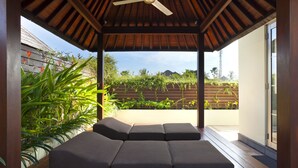 A covered outdoor seating area with a ceiling fan, wooden flooring, and a view of a garden and mountains in the background. - Sun Island Boutique Villas & Spa Seminyak (Seminyak)