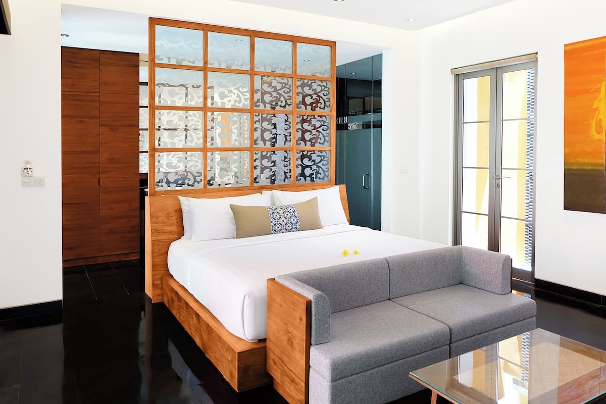 Habitación de hotel moderna con una cama de madera, un sofá gris, una mesa de centro de vidrio y un amplio ventanal con vistas.