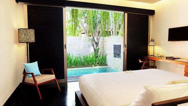 A hotel room with a bed, a desk, a chair, a TV, and a view of a pool and greenery. - Sun Island Boutique Villas & Spa Seminyak (Seminyak)