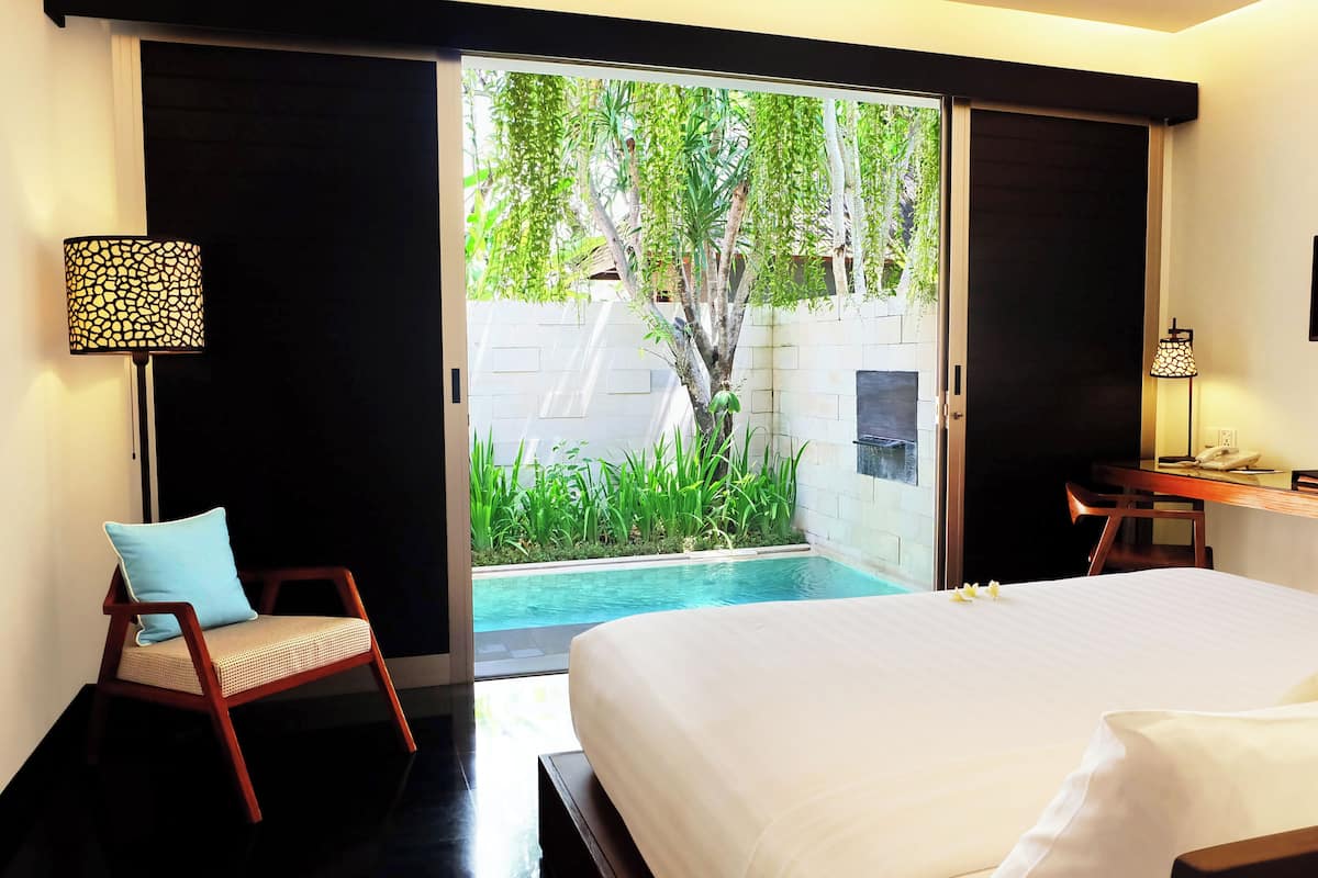 Habitación de hotel con cama, escritorio, silla, televisor y vistas a una piscina y zonas verdes.