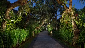 A pathway flanked by lush greenery and trees, leading towards a building. - Sun Island Boutique Villas & Spa Seminyak (Seminyak)