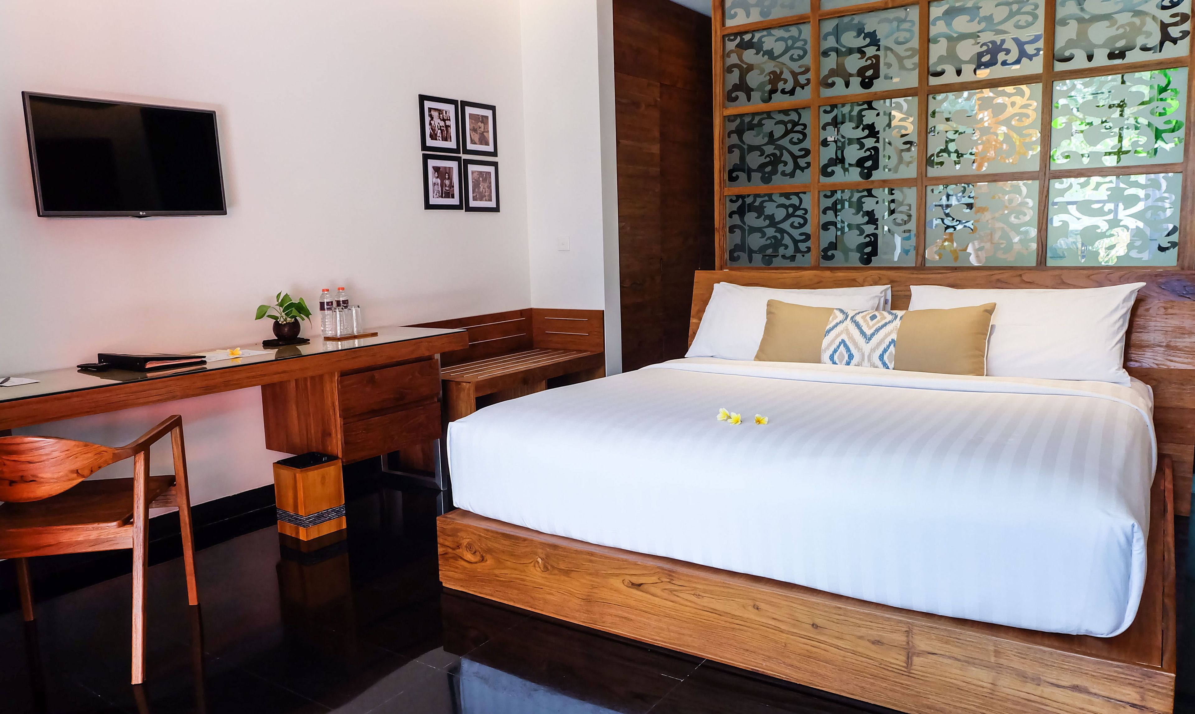 Habitación de hotel con cama, escritorio, silla, televisor y ventana con vidrio decorativo.