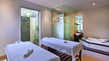 Relax in a serene spa room with two massage tables, a bathtub, and a large mirror.