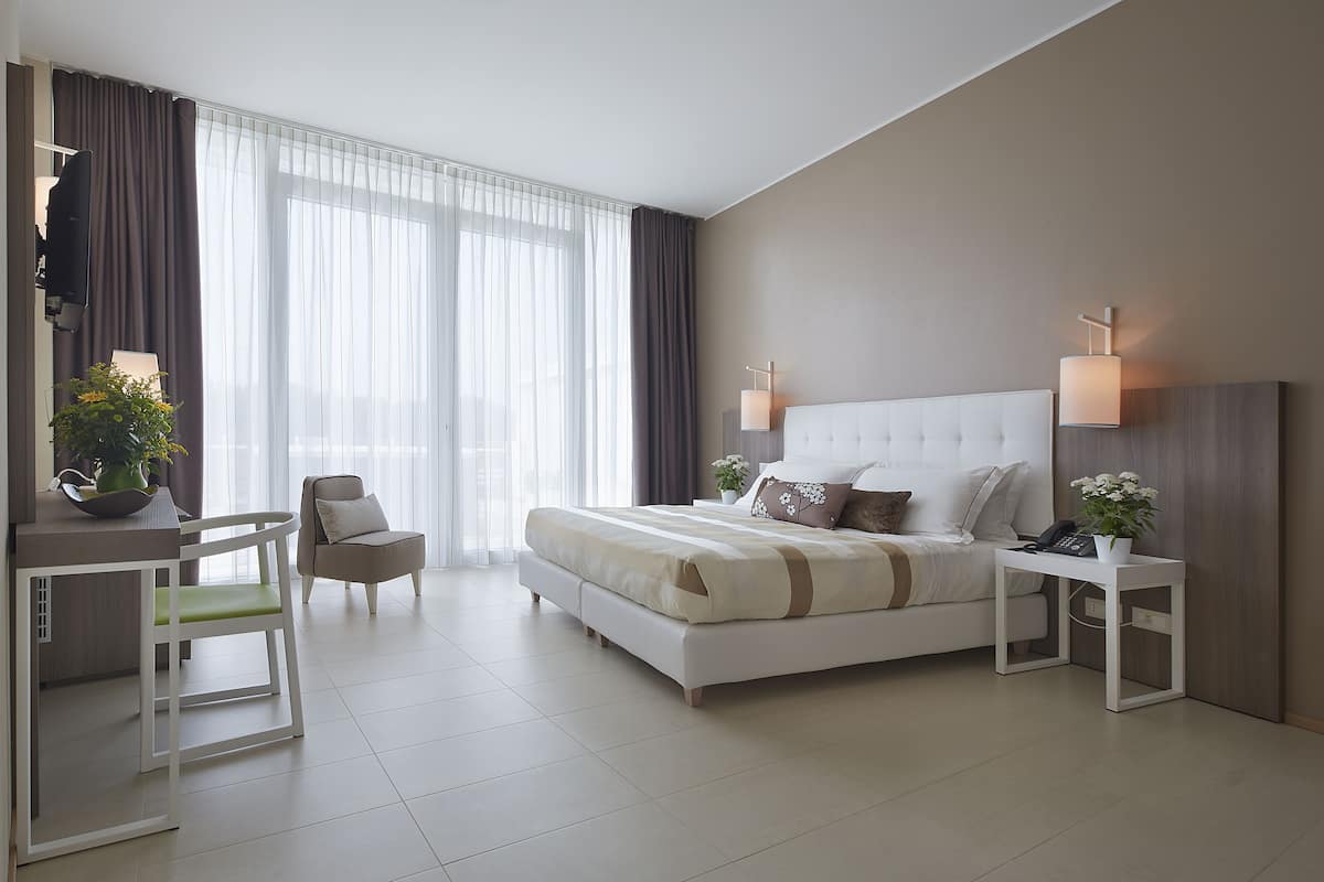 Quarto de hotel moderno com uma cama grande, mesas de cabeceira, escrivaninha e uma cadeira.