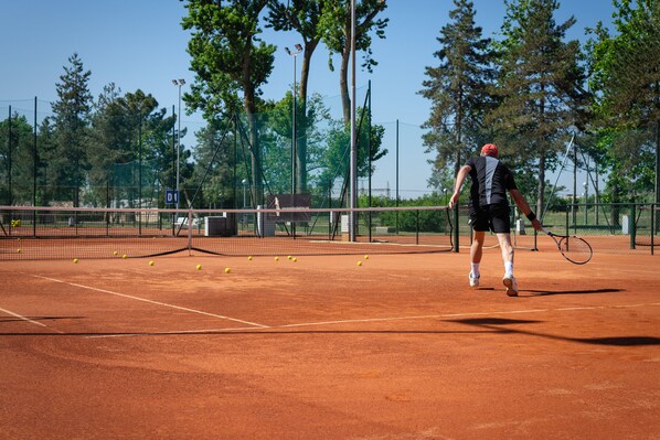 A tennis court with a net, trees, and a clear sky. -  Isola di Albarella Hotel Capo Nord (Rosolina)