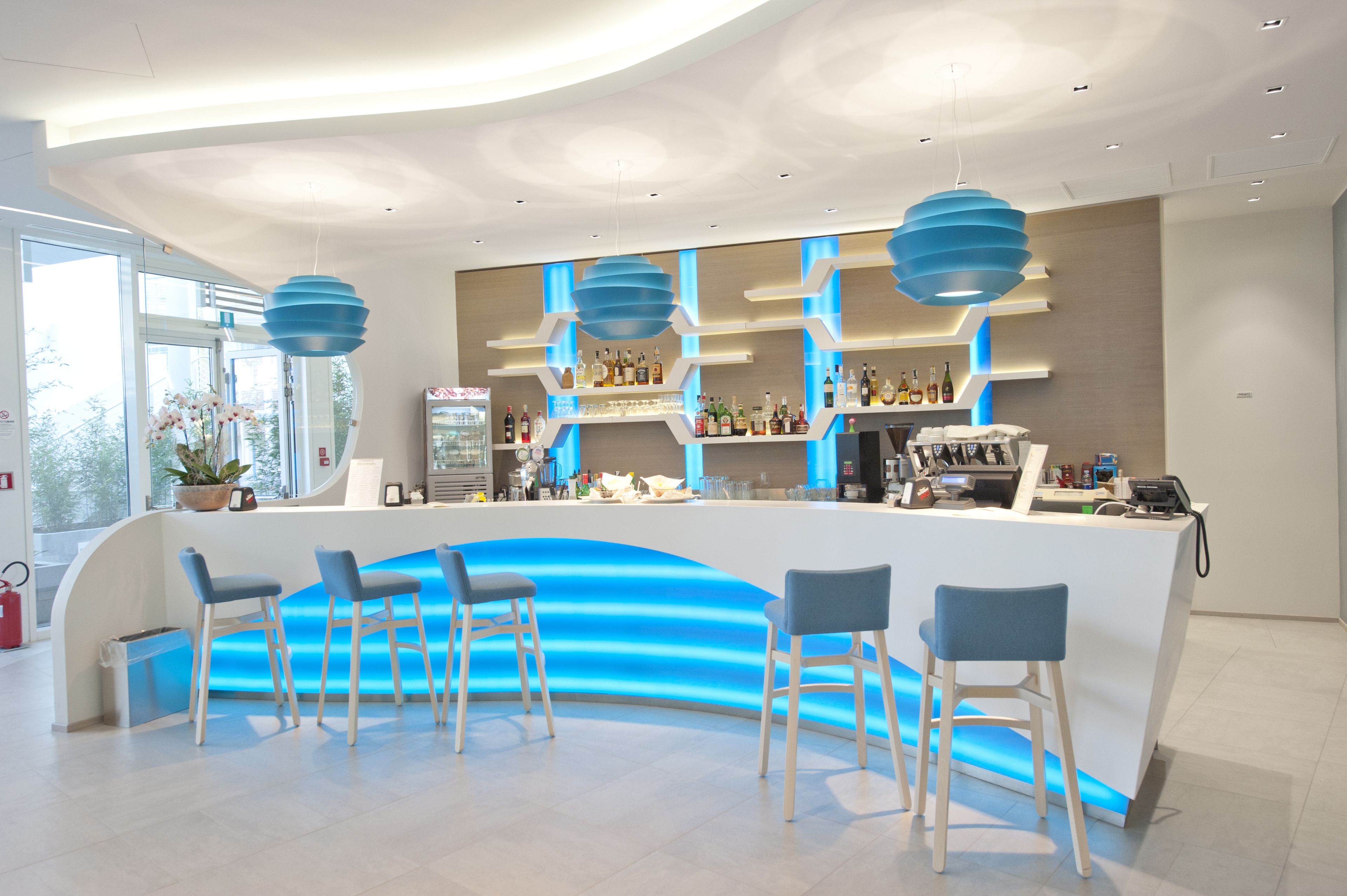 Un área de bar moderna con una barra curva, detalles de iluminación azul y varios taburetes.