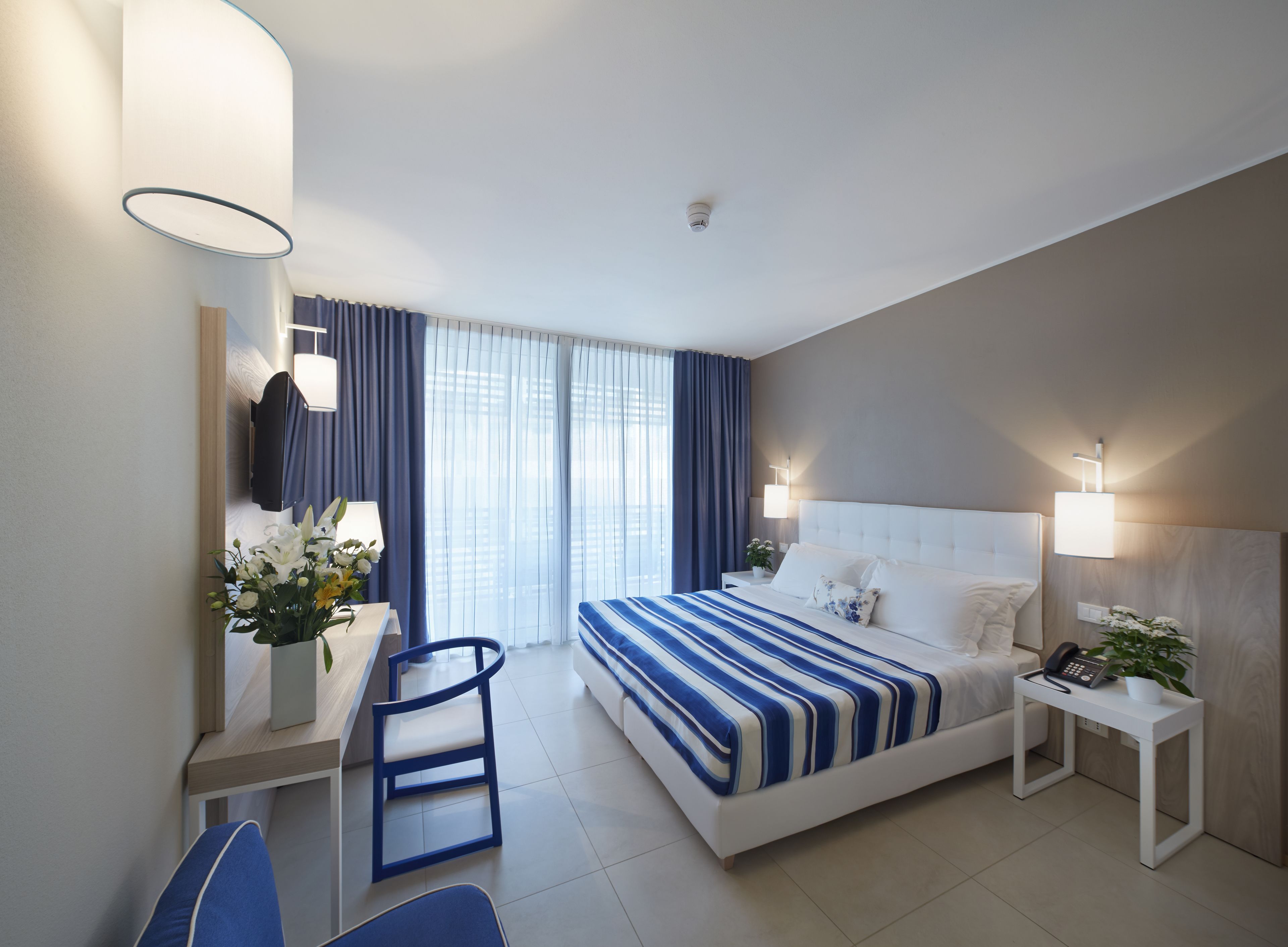 Une chambre d’hôtel comprenant un lit, des tables de chevet, un bureau, une chaise et des rideaux.