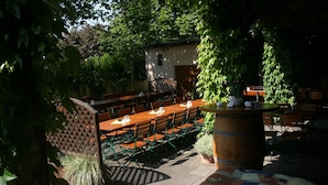 An outdoor dining area with wooden tables and chairs, surrounded by greenery and a small building in the background. - Hotel Odenwaldblick (Roedermark)