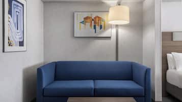 Quarto de hotel moderno com um sofá azul, uma luminária e duas obras de arte na parede.