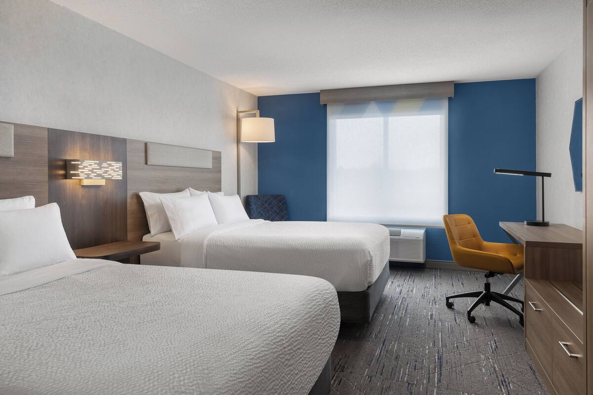 Una habitación de hotel con dos camas, un escritorio, una silla, una lámpara y una ventana.